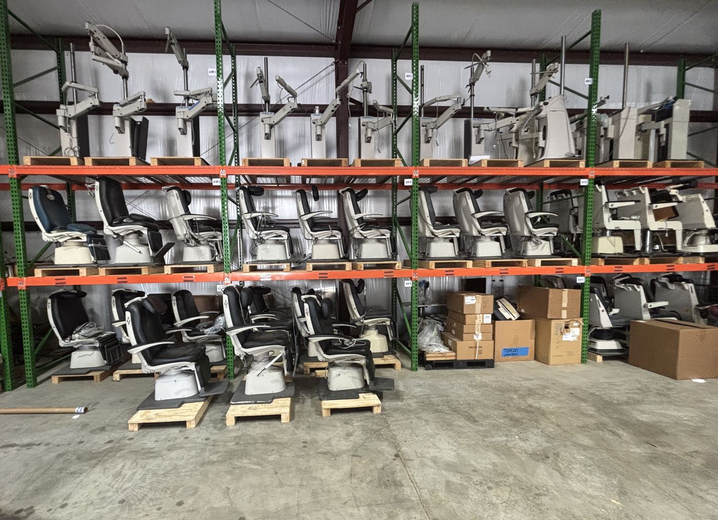 More rows of exam chairs and instrument stands on pallet racking in a warehouse